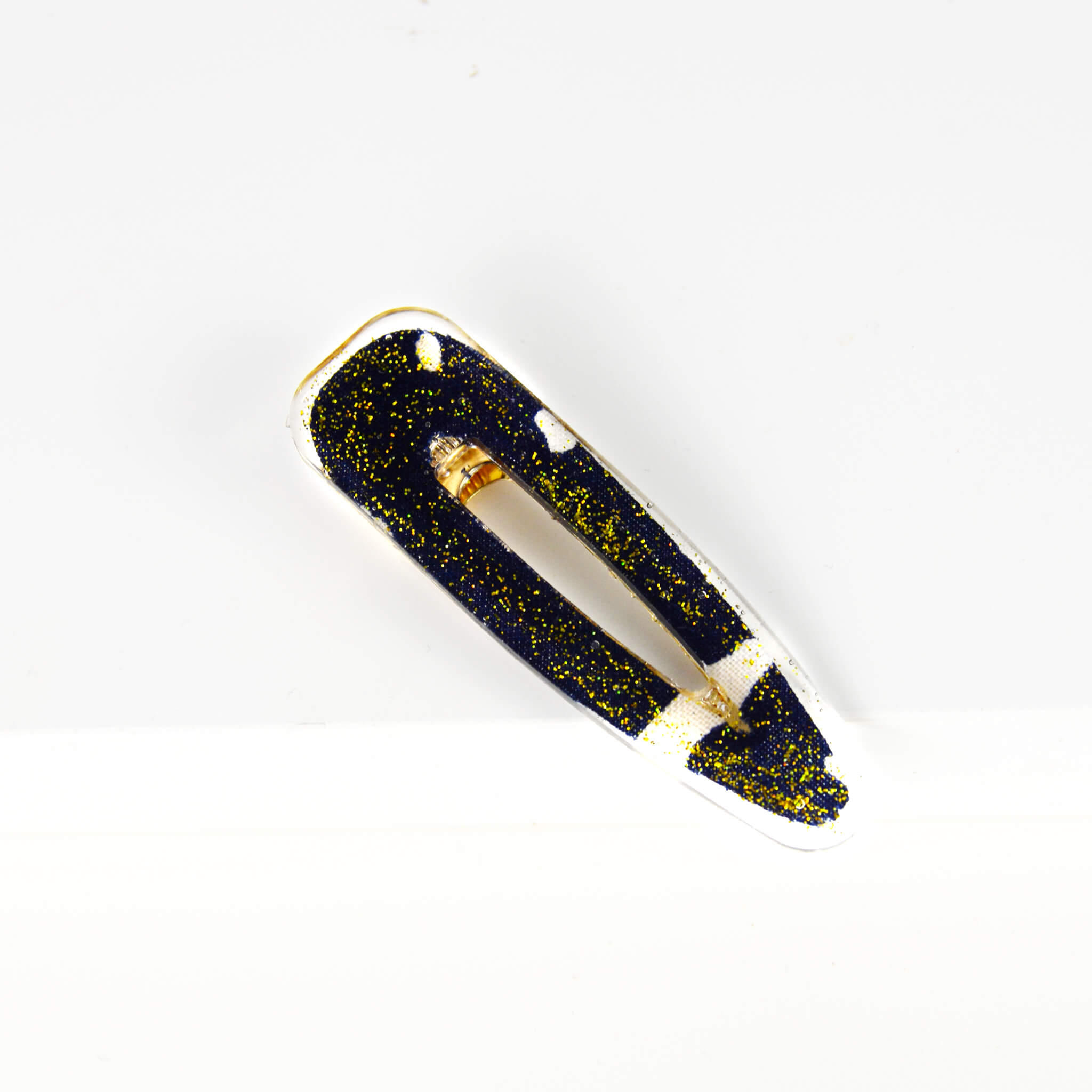 barrette en forme de goutte de larme faite en résine encastrant un retaille de tissu africain bogolan bleu et blanc et des paillettes dorées
