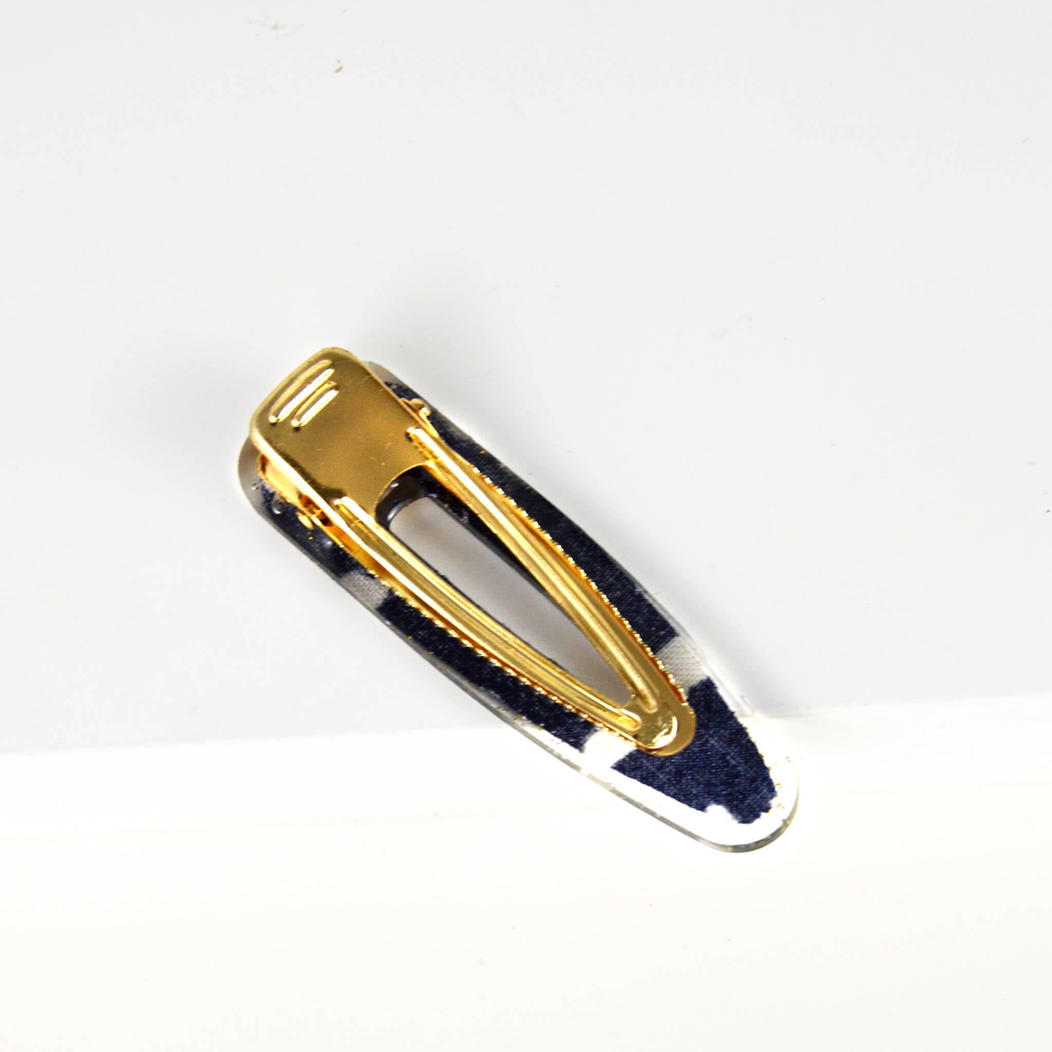 handmade ecodriendly teardrop barrette made of blue and white african print mud cloth fabric and resin containig gold glitter equiped with an alligator clip 