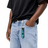 Porte-clé en tissu turquoise et noir accroché à un jean porté par un modèle homme, vue rapprochée, Québec Coo-Mon
