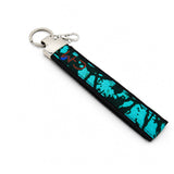 Porte-clé en tissu turquoise et noir posé sur fond blanc, Québec Coo-Mon